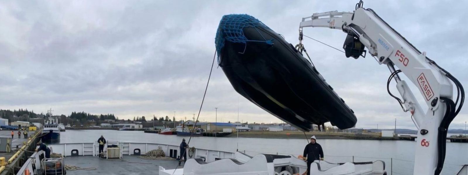 Grúa marina Fassi F50 montada en una embarcación, izando un bote inflable con eslinga sobre cubierta.